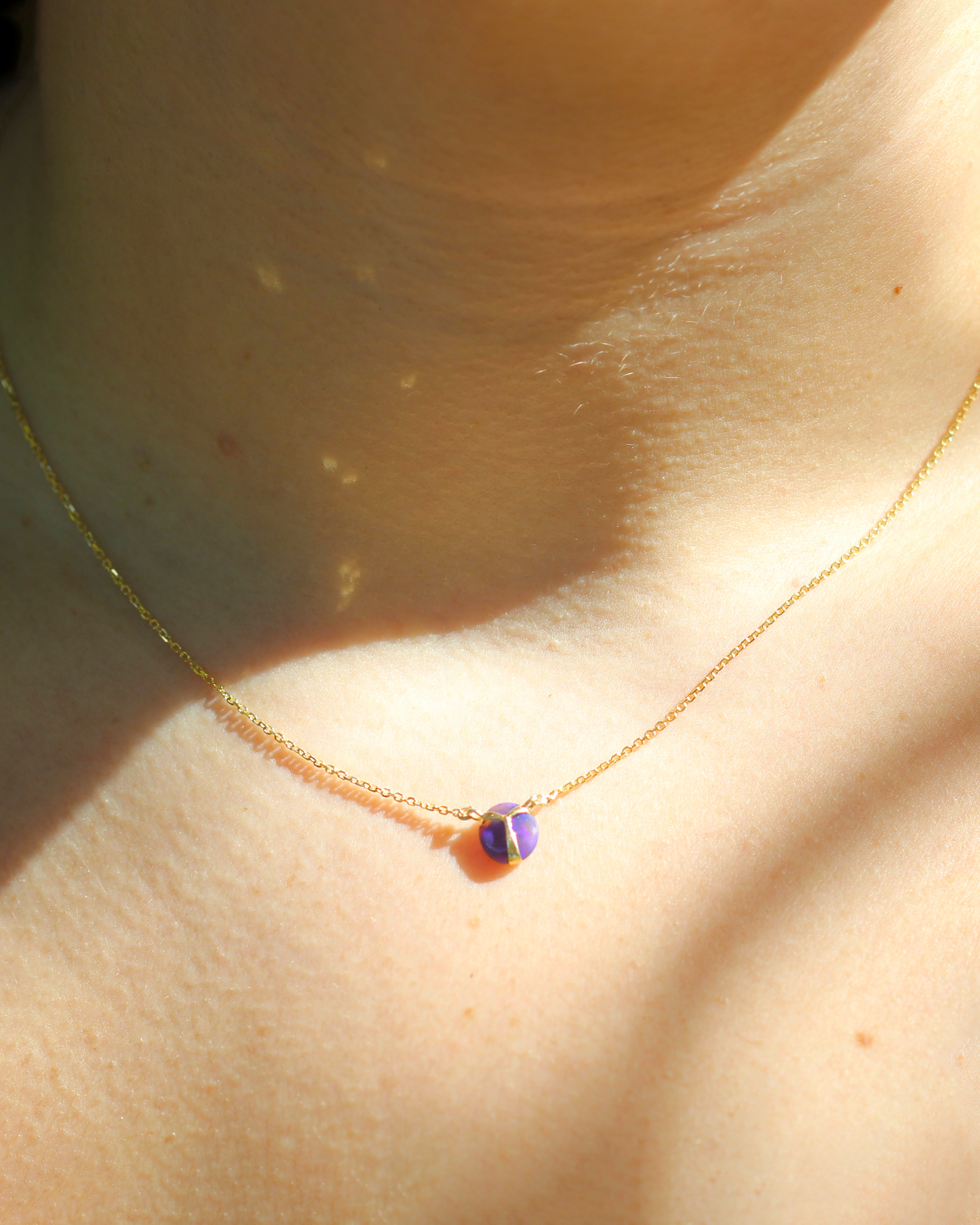 Closeup of woman wearing Deep Purple colored opal pendant necklace with yellow gold beetle wing detail, on a yellow gold chain