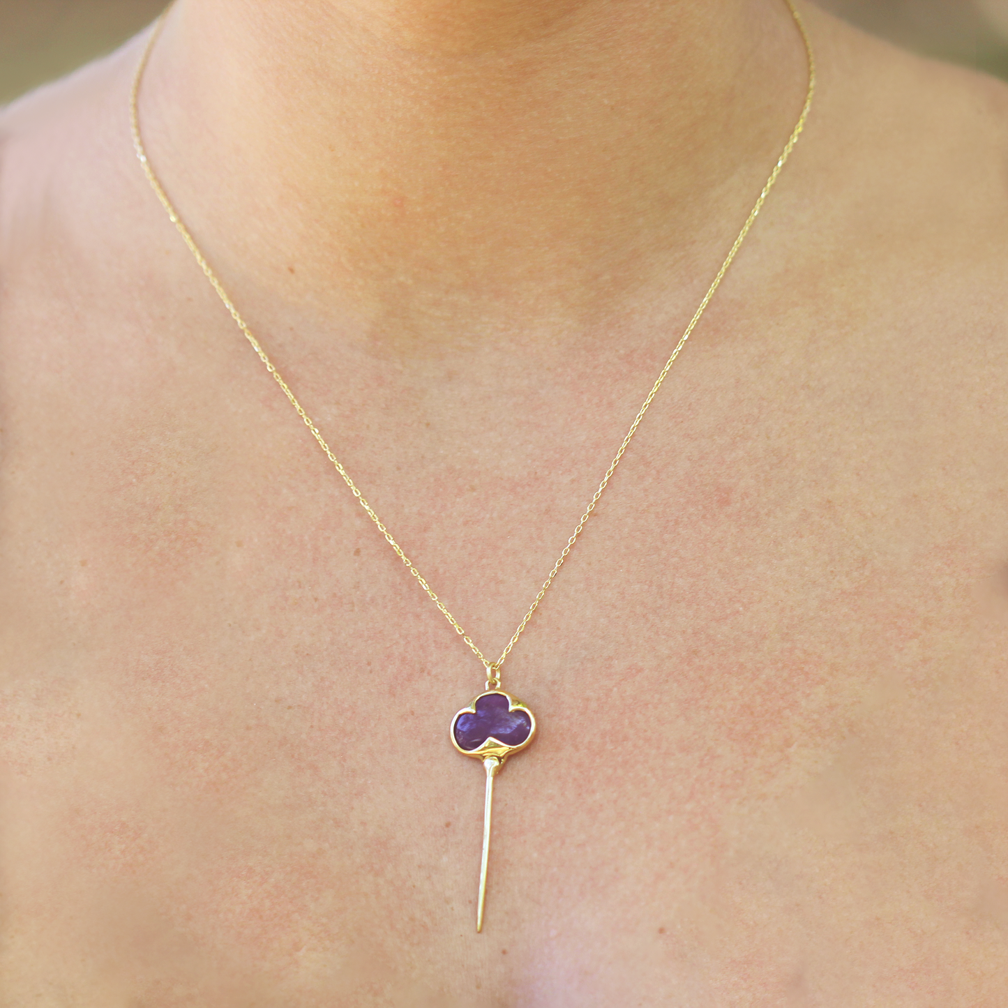 Woman modeling Yellow gold necklace with bezel set purple sugilite stone, and an elongated gold stingray tail dangling from the bottom, on a dainty gold chain