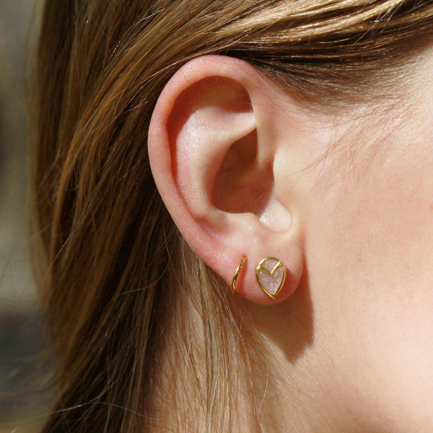 Woman wearing stud earring with teardrop-shaped, white druzy quartz stone, bezel set with yellow gold owl beak detail