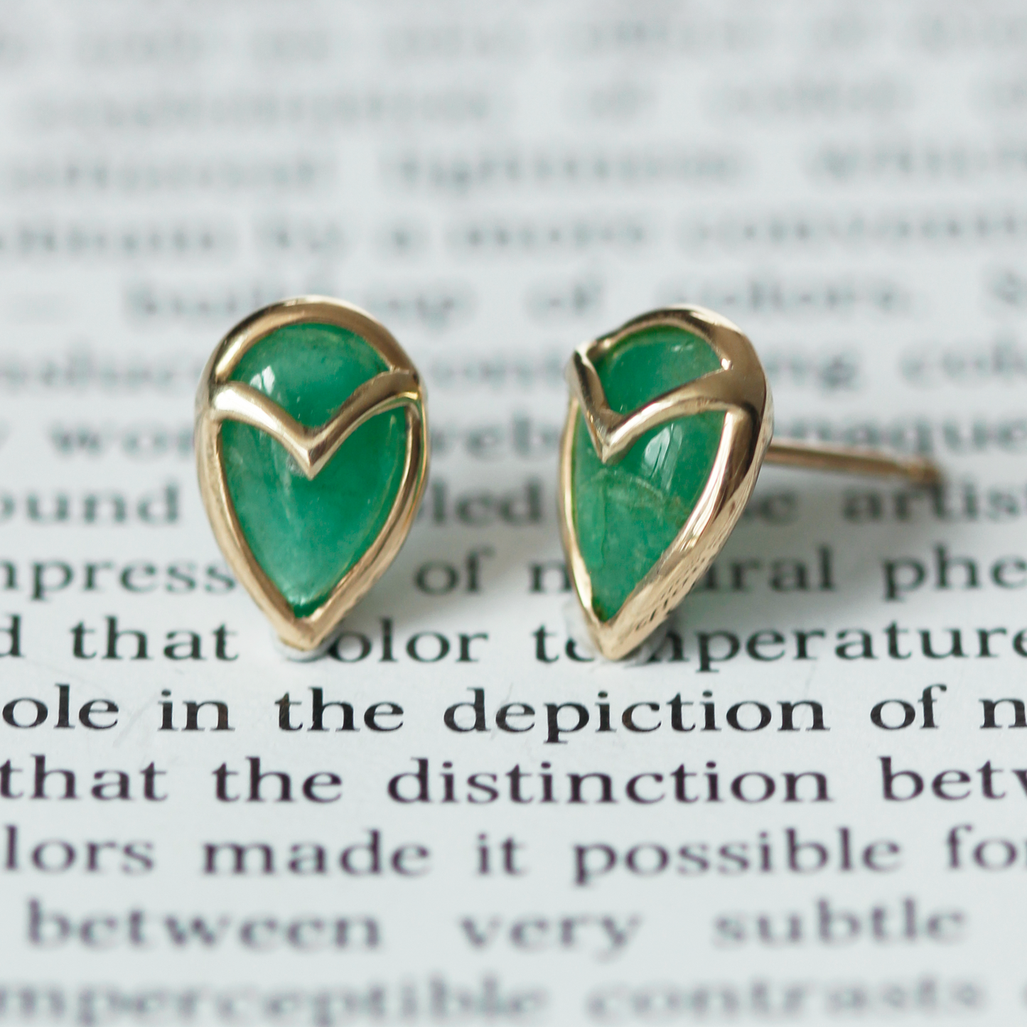 A pair of stud earrings with teardrop-shaped, green emerald stone, bezel set with yellow gold owl beak detail