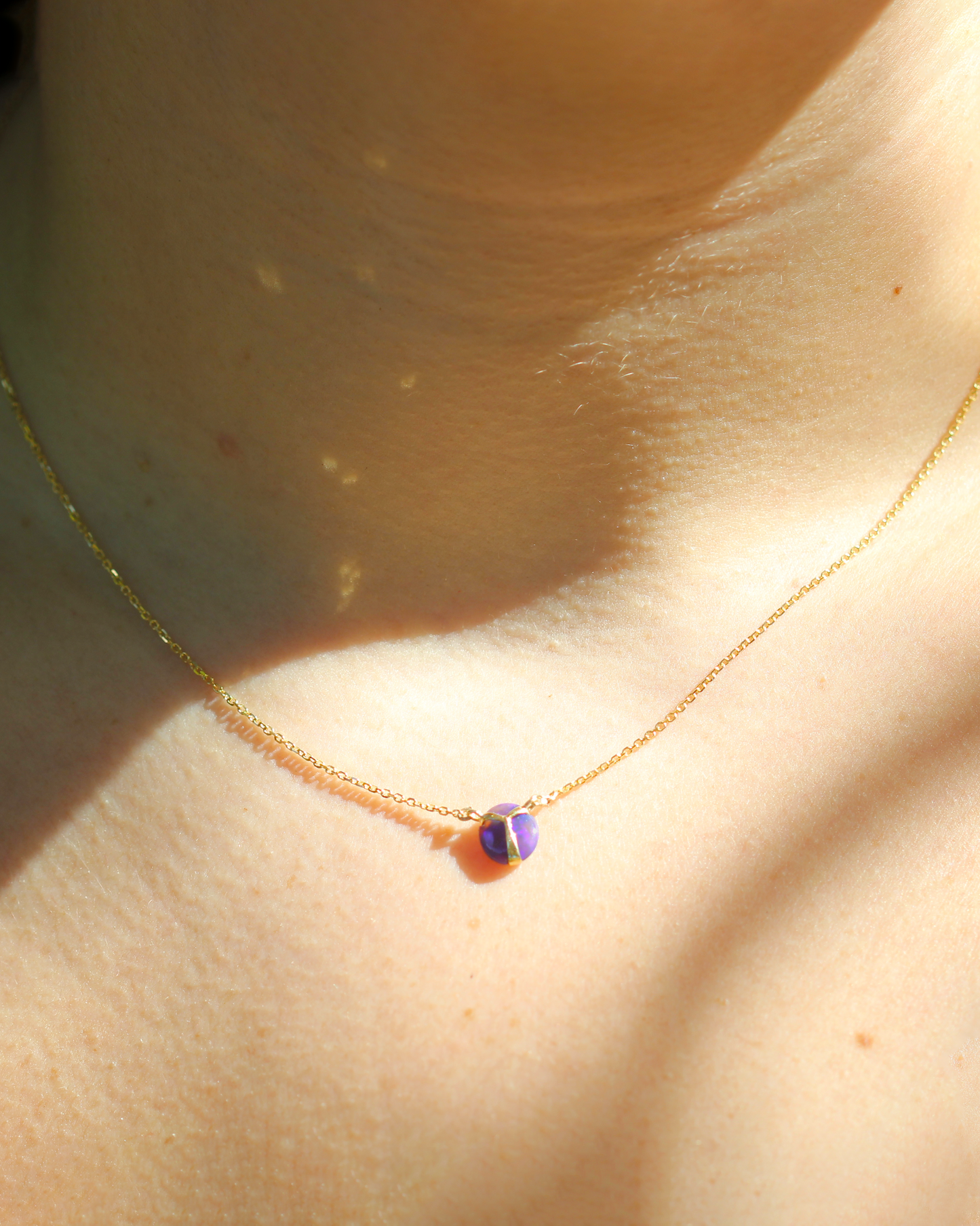 
                  
                    Closeup of woman wearing Deep Purple colored opal pendant necklace with yellow gold beetle wing detail, on a yellow gold chain
                  
                