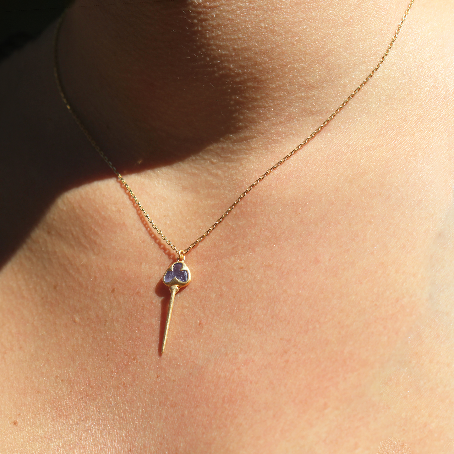 
                  
                    Woman wearing Yellow gold necklace with bezel set, pale purple tanzanite stone, and an elongated gold stingray tail dangling from the bottom, on a dainty gold chain
                  
                