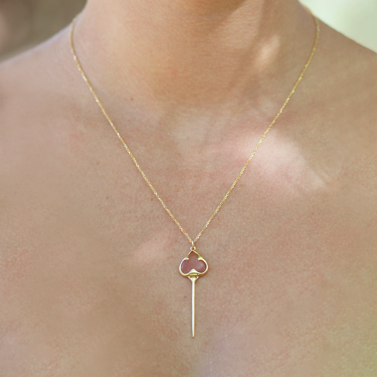 
                  
                    Woman wearing Yellow gold necklace with bezel set muted pink guava quartz stone, and an elongated gold stingray tail dangling from the bottom, on a dainty gold chain
                  
                