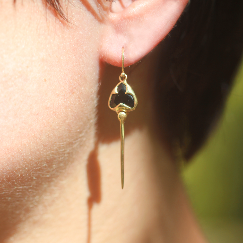 Woman modeling Yellow gold earrings with french hooks, bezel set black onyx stones, and an elongated stingray dangling from the bottom