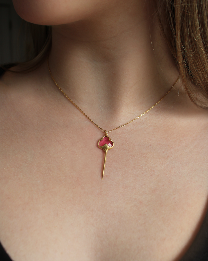 Woman wearing Yellow gold necklace with bezel set pink tourmaline stone, and an elongated gold stingray tail dangling from the bottom, on a dainty gold chain