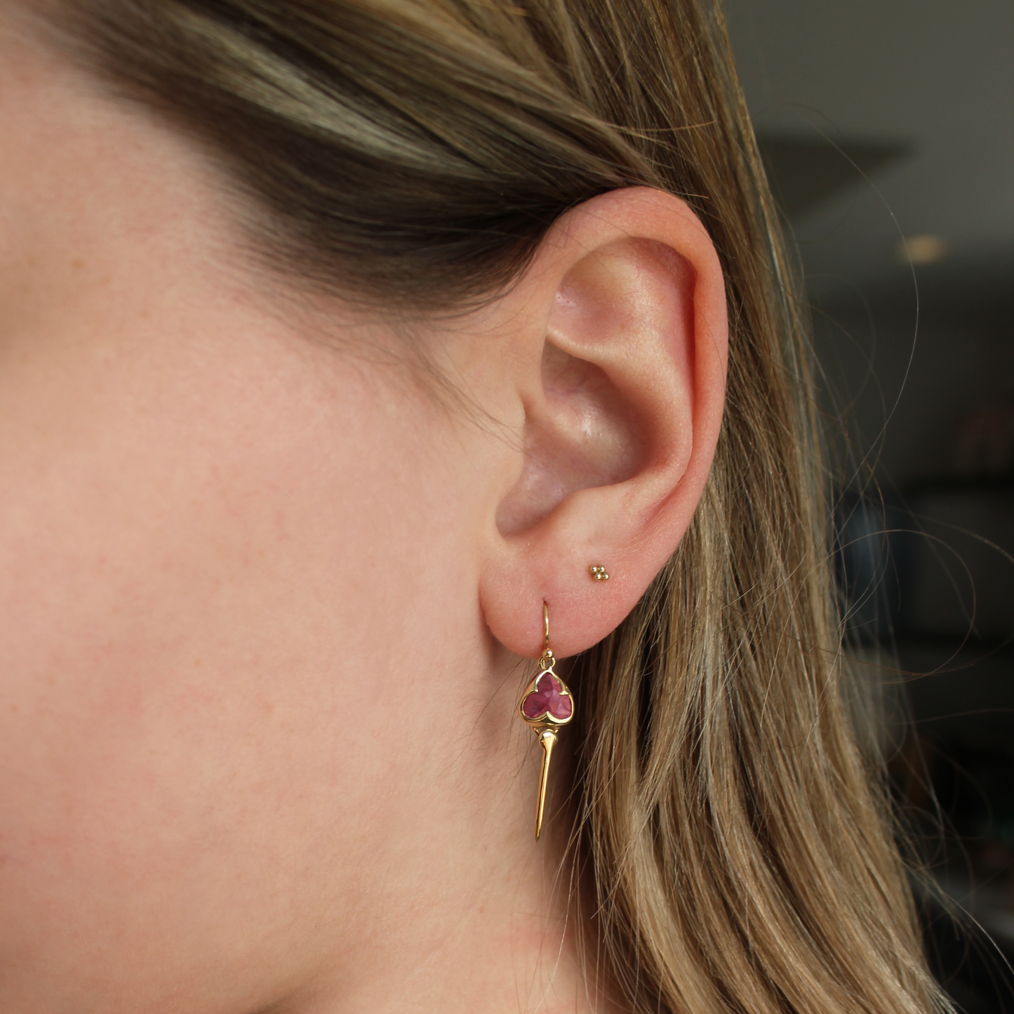 Woman wearing Yellow gold earrings with bezel set pink tourmaline stone, and an elongated gold stingray tail dangling from the bottom
