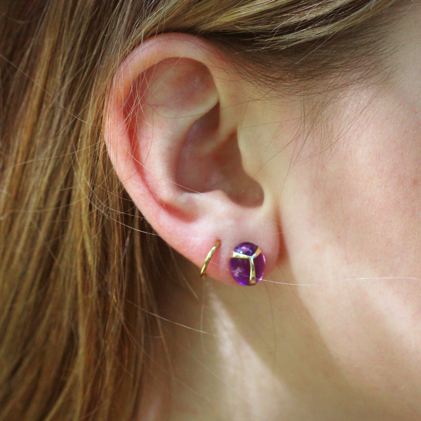 Model wearing A pair of amethyst stud earrings with yellow gold beetle wing detail.